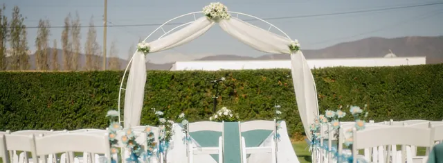 Arco de ceremonia con flores y sillas blancas sobre el pasto