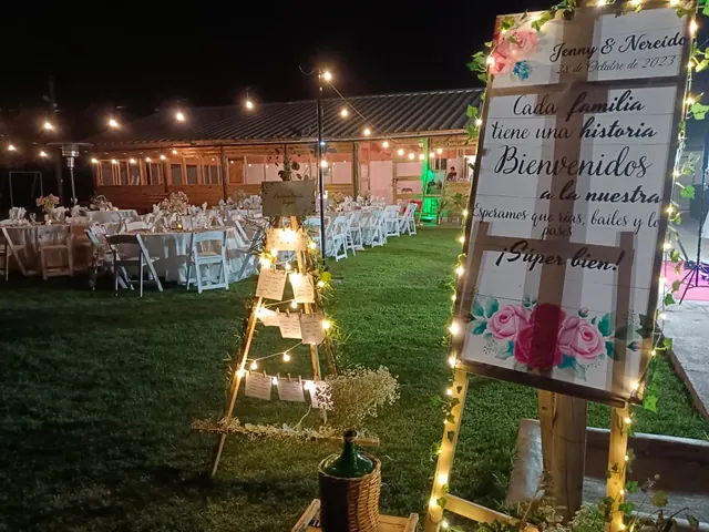 Recepción nocturna al aire libre con cartel de bienvenida y guirnaldas de luces